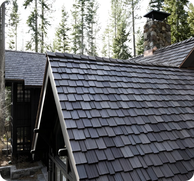 An A-frame wooden house with a brown shingle roof, crafted by expert roofing companies, features a stone chimney and is nestled among tall pine trees.