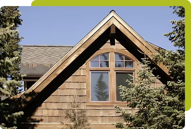 A-frame wooden house exterior with expertly installed shingled siding, arched windows, and surrounding evergreen trees showcases perfect roof installation.